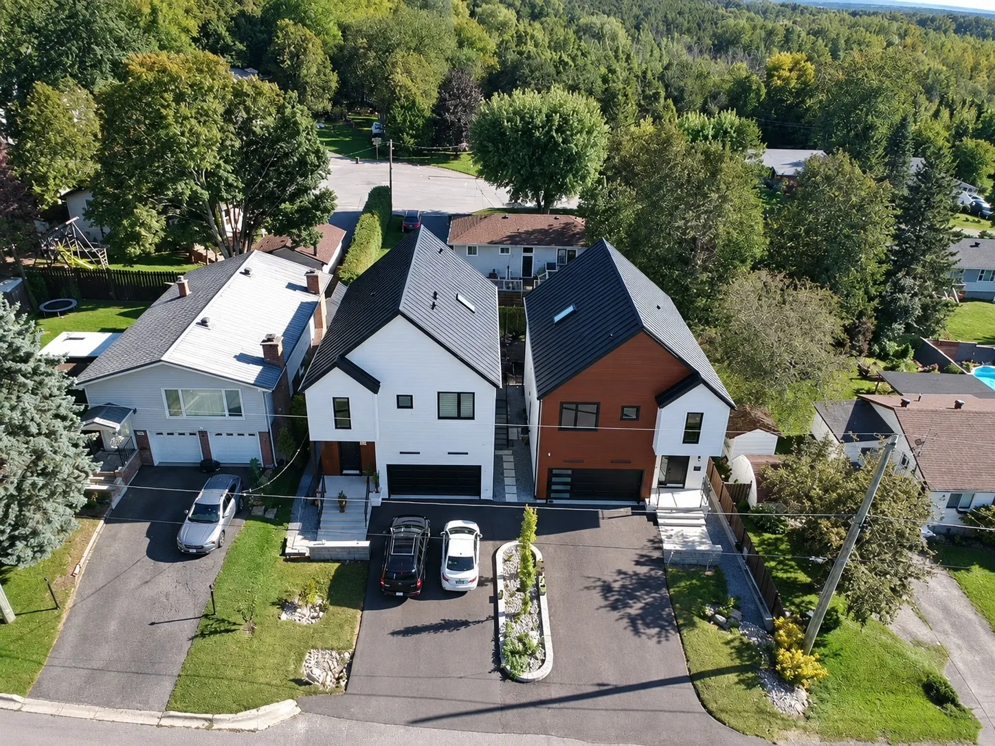 From the air in front of the house: the two gables of the house and its neighbour, the driveways, cars, the trees behind