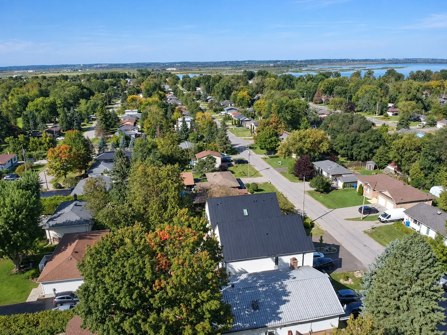 From the air: the house and its street below, the rooftops and trees of Keswick, and the water of Lake Simcoe on the horizon at the right