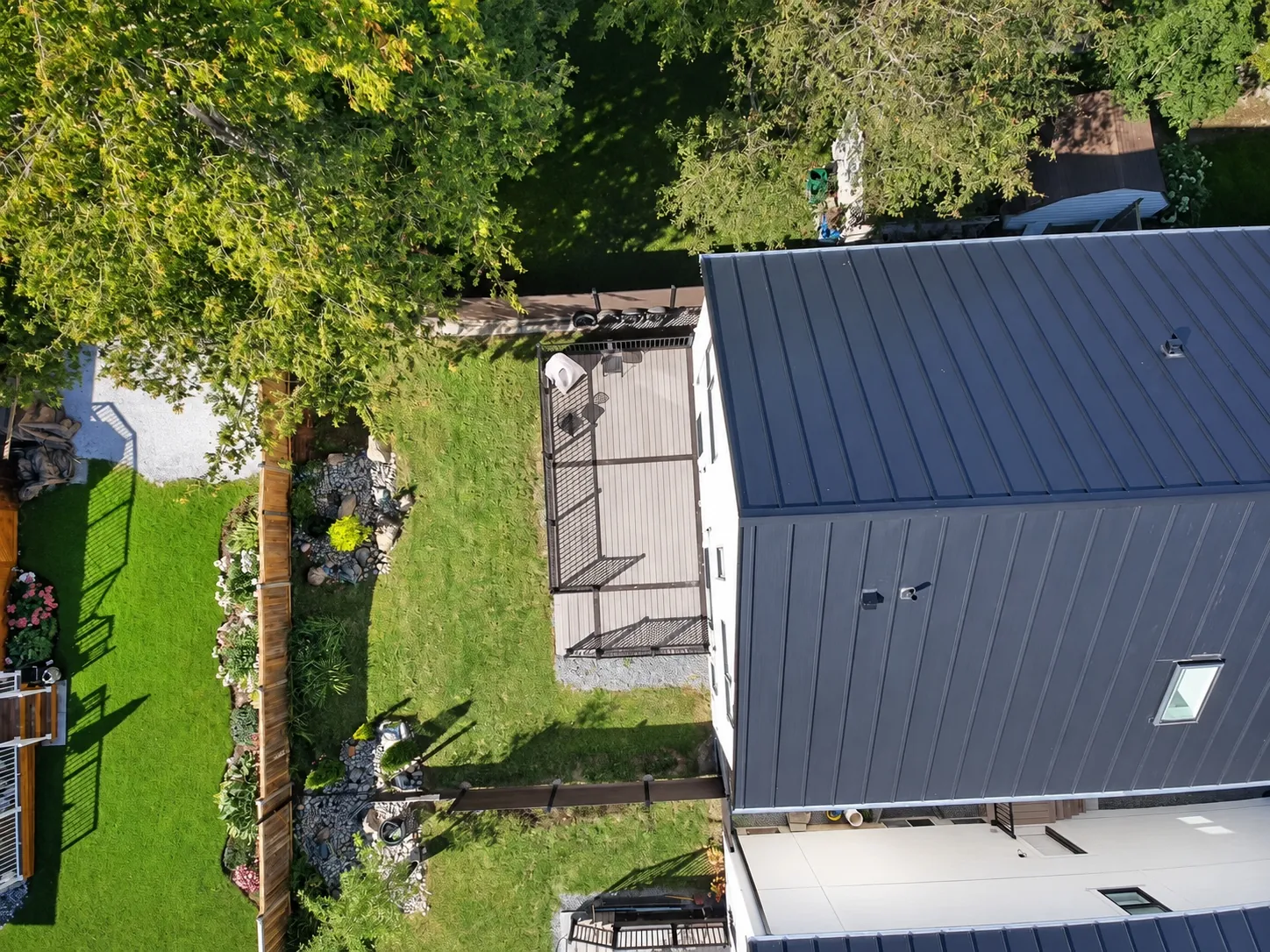 Straight down onto the back of the house: the metal roof, the deck, the lawn and the fence, the neighbours' yards