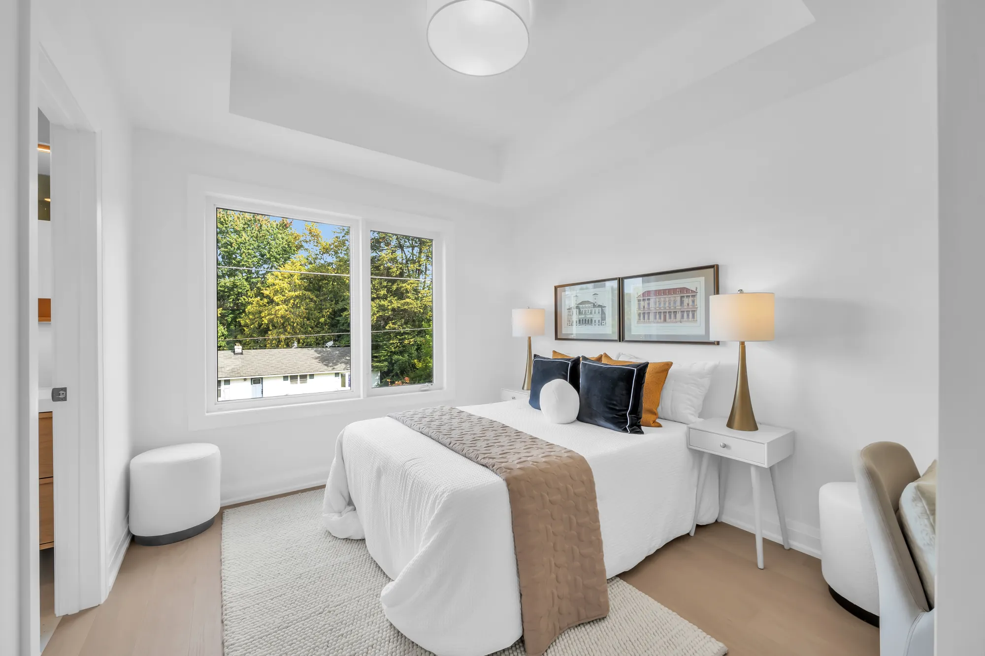 A third bedroom: a bed with white linen and navy cushions under two framed prints, a window, a desk chair, a tray ceiling