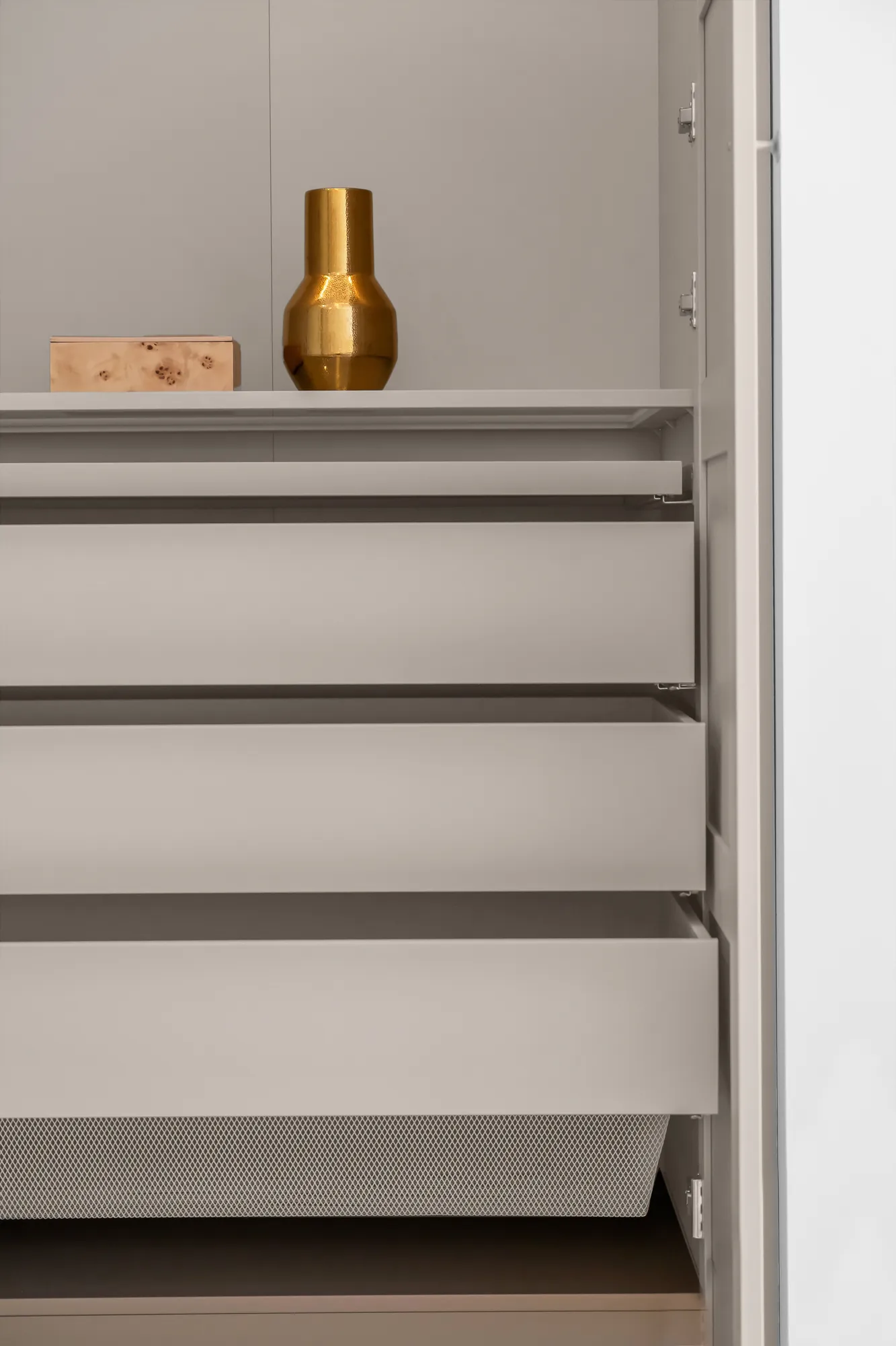 A detail of the walk-in closet: white shelves and drawers, a brass vase