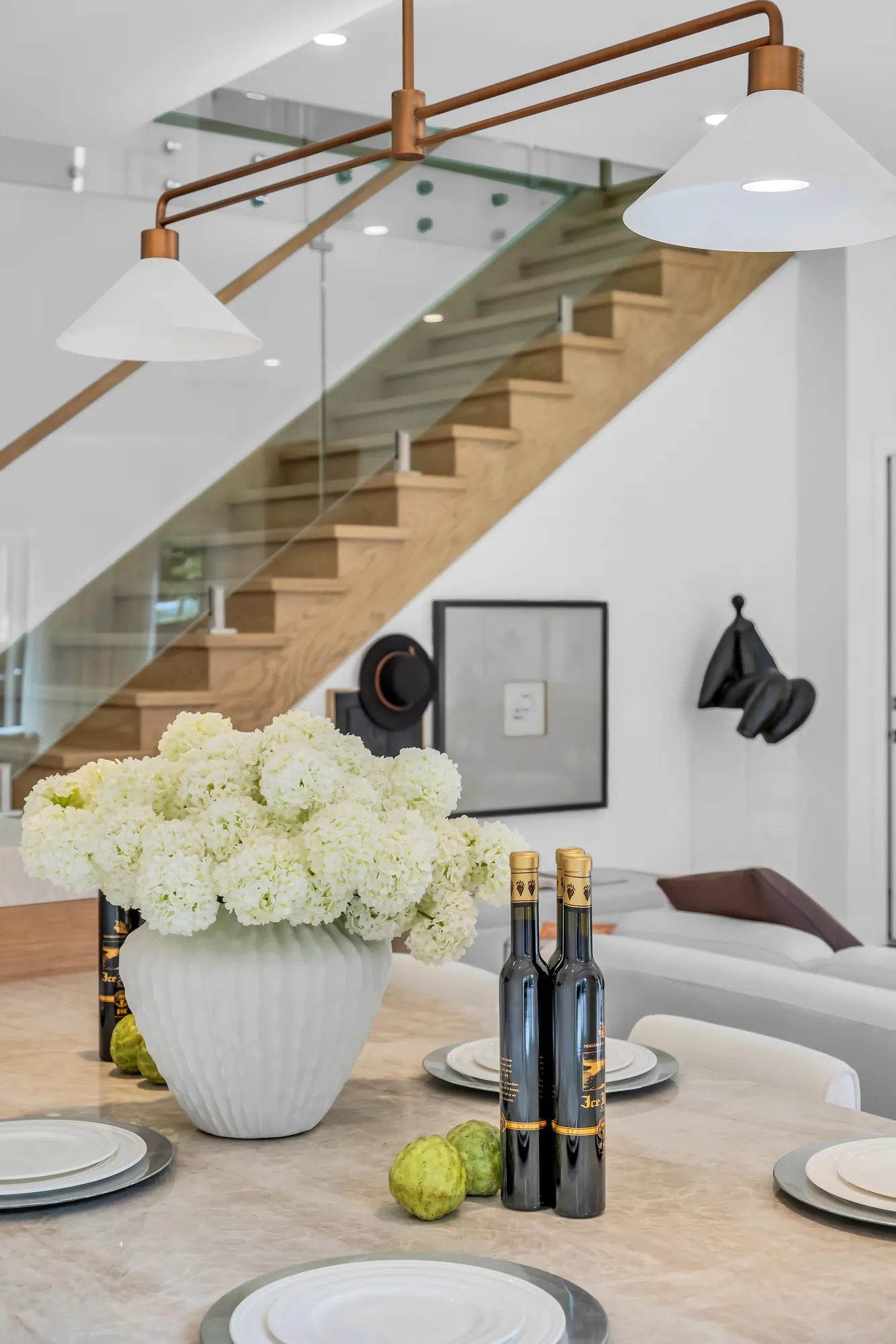 The island set for dinner under its pendant, the stair's oak treads and glass rail rising behind