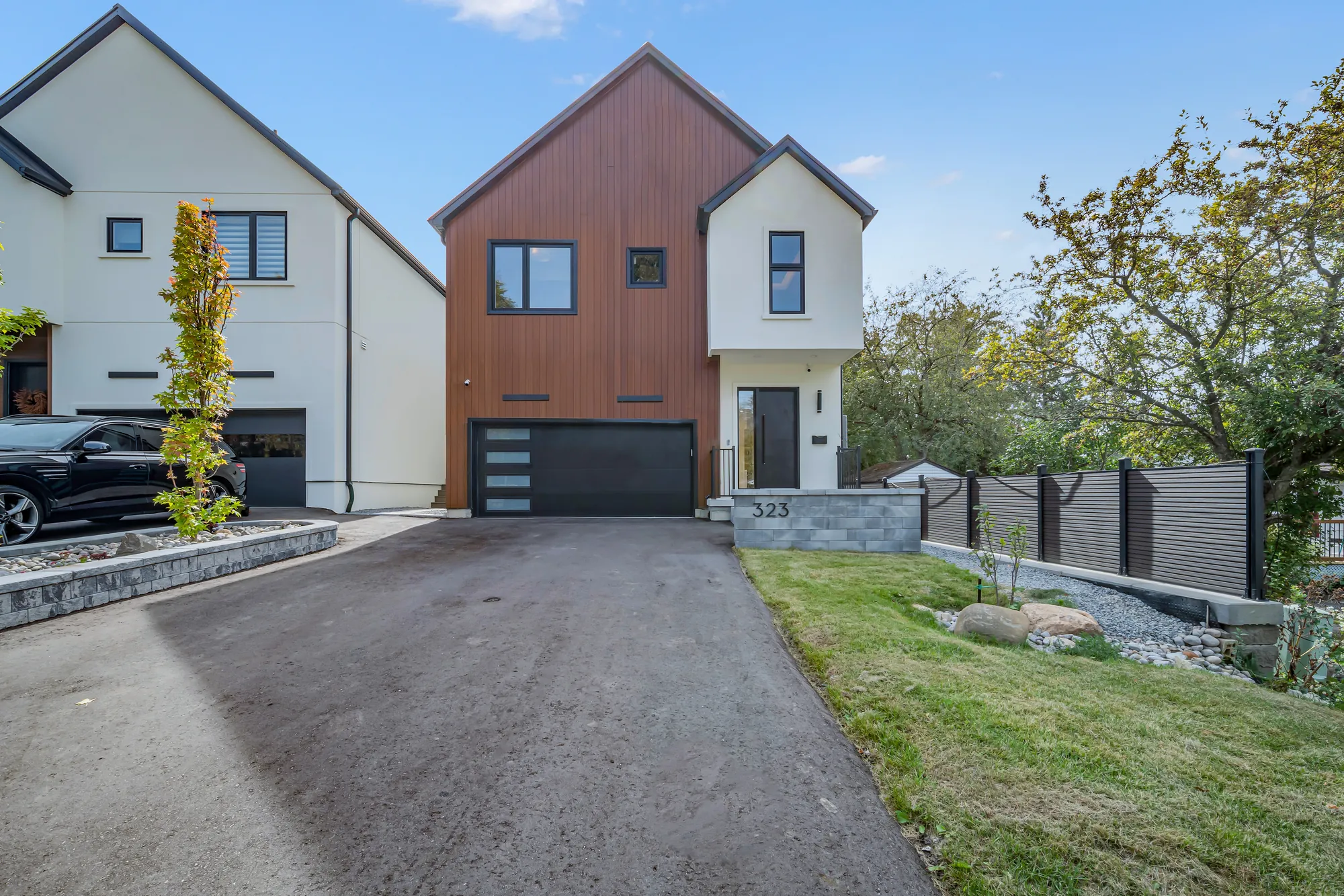 The house from the foot of the driveway: the asphalt drive to the garage, a strip of lawn and a stone wall at the right, the neighbouring house at the left, trees behind