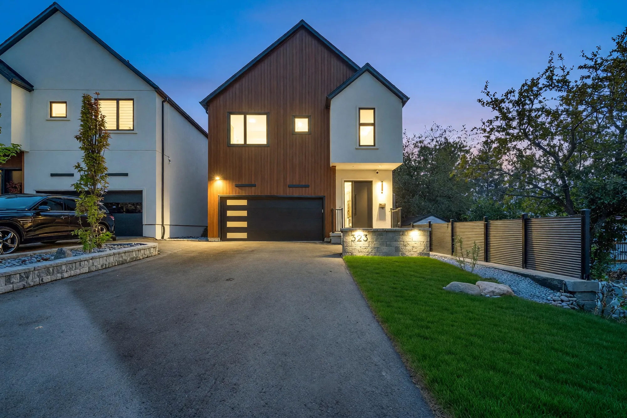 The same view from the foot of the driveway at dusk, the windows lit and the lawn shown green