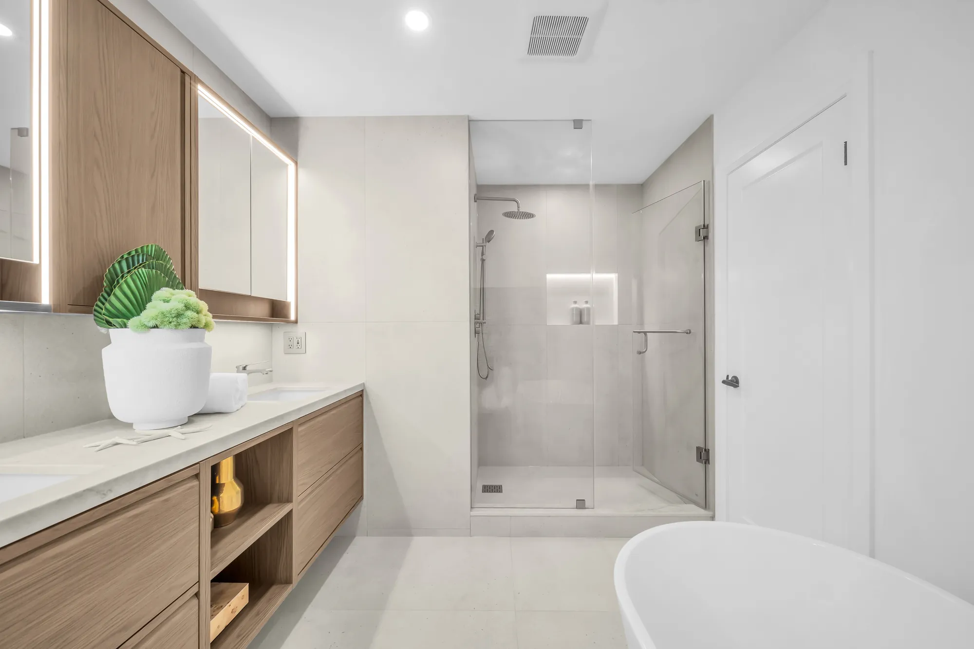 The primary ensuite from the vanity: the glass shower with a rain head, the tub, the door