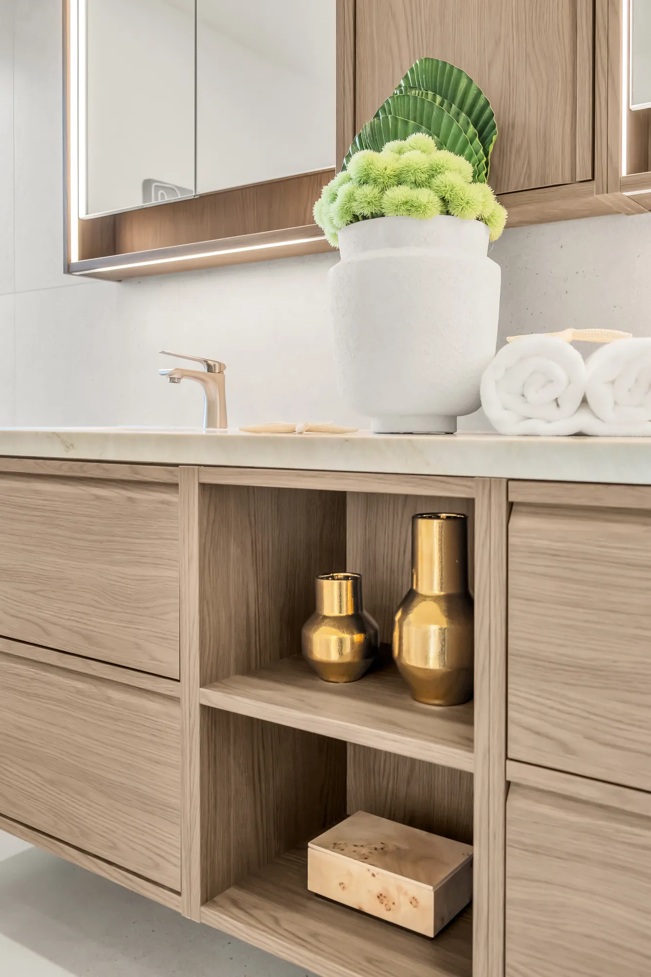 A detail of the ensuite vanity: oak drawers and open shelves, brass objects, a white basin