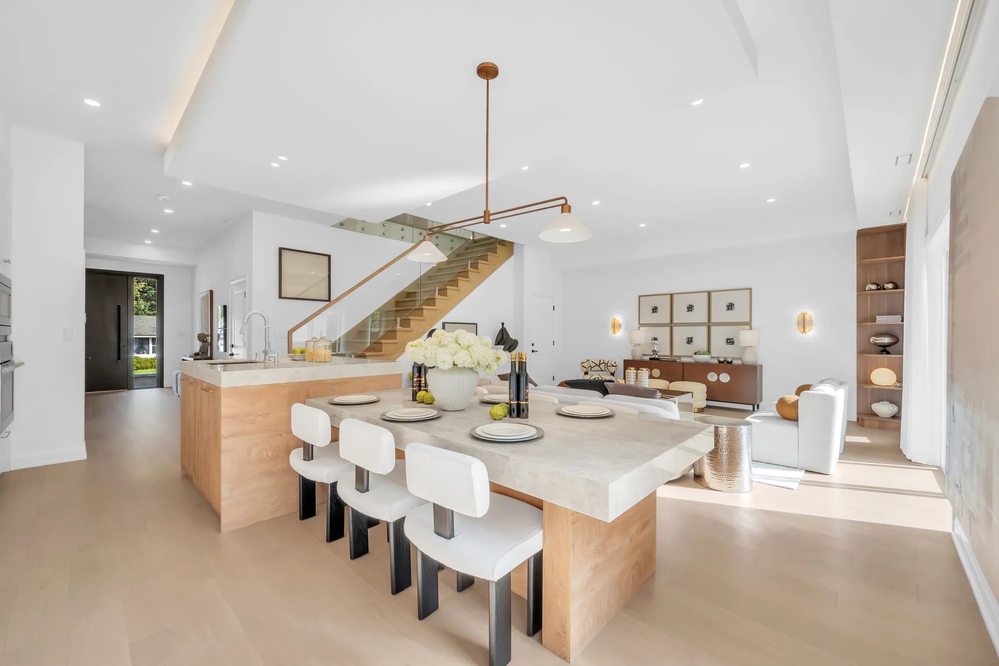 The island from the living room: white stools, hydrangeas and bottles on the stone counter, the stair beyond, a pendant above