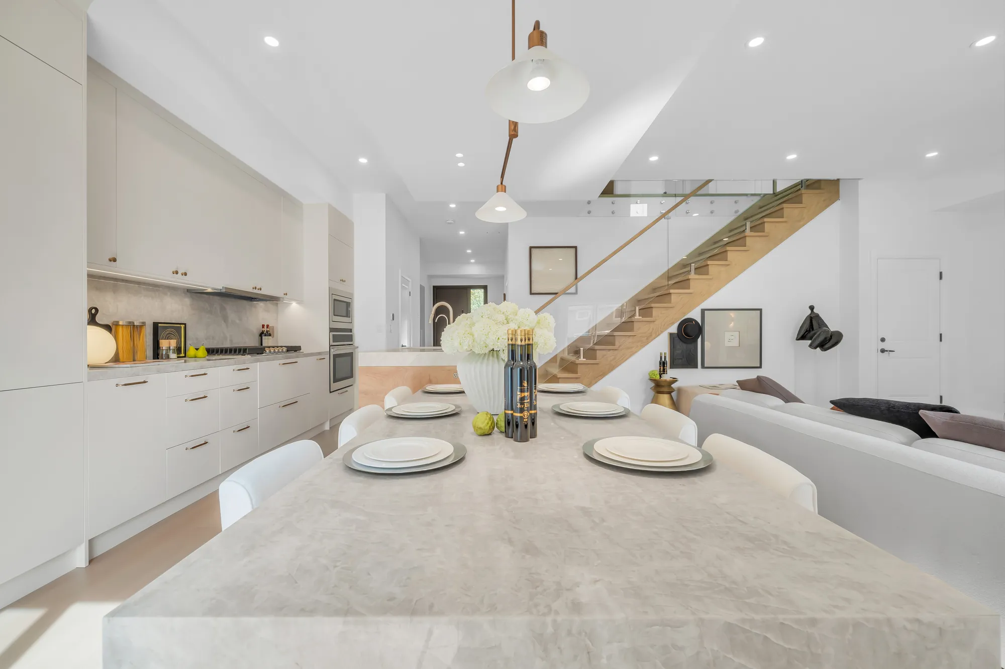 The island from its end: the stone counter set with plates, the stair with its glass rail beyond, the living room to the right