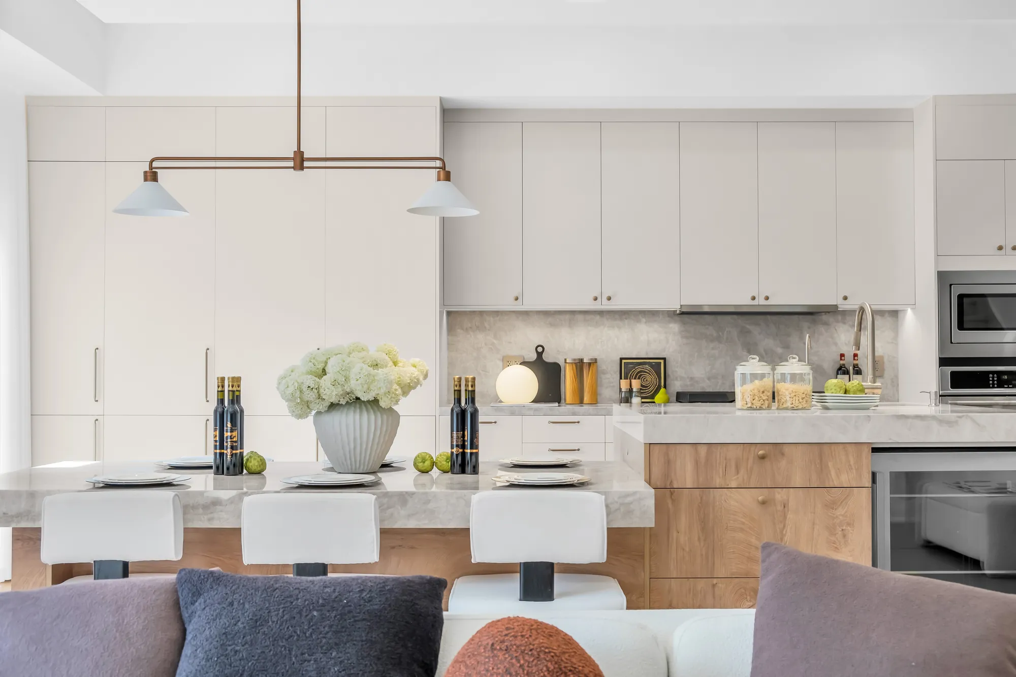 The kitchen from the living room sofa: the island, the pendant, the white cabinets and the ovens