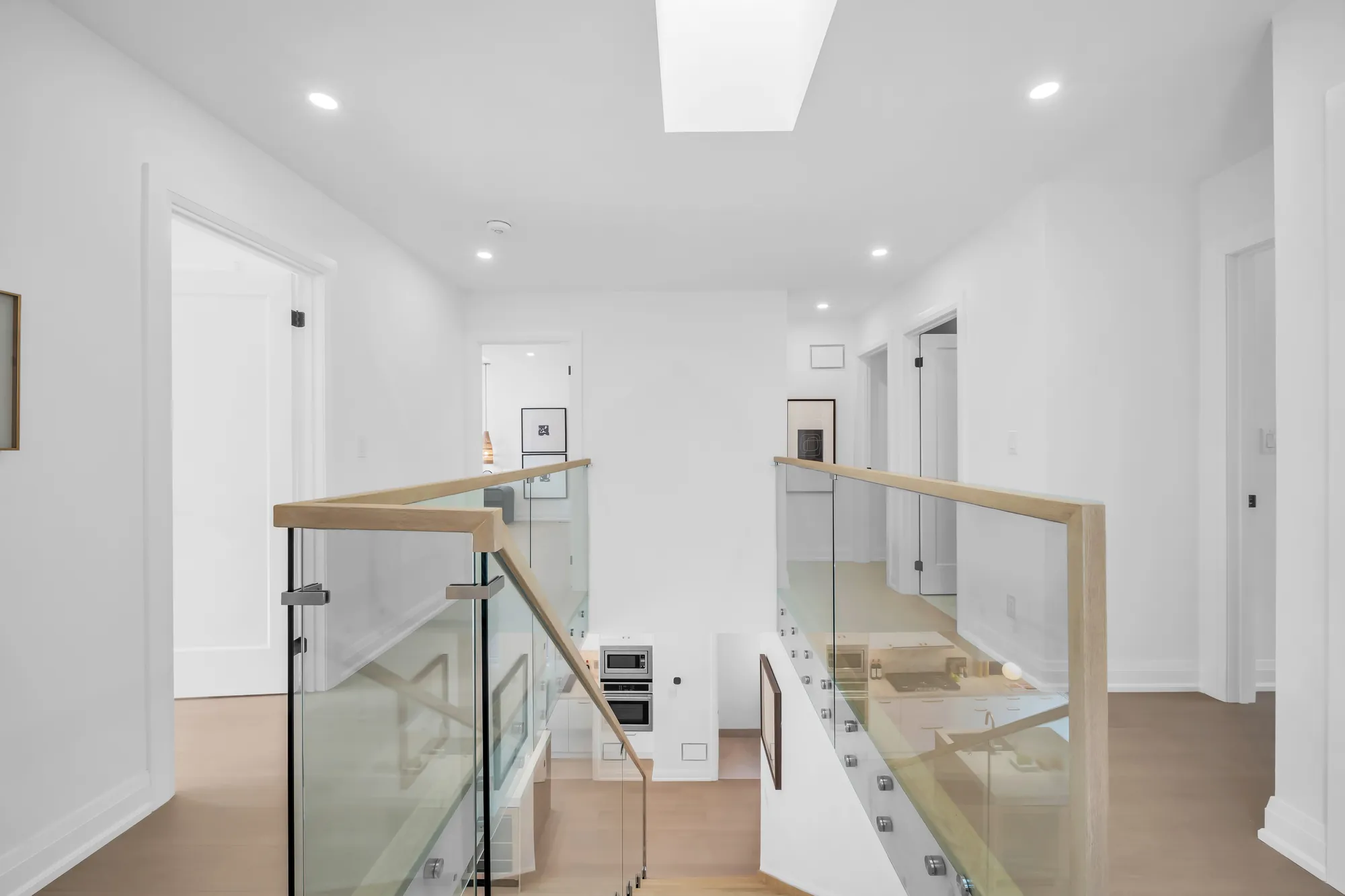 The upper landing: a skylight in the ceiling, the glass railing with its oak handrail, doors to the bedrooms, oak floors