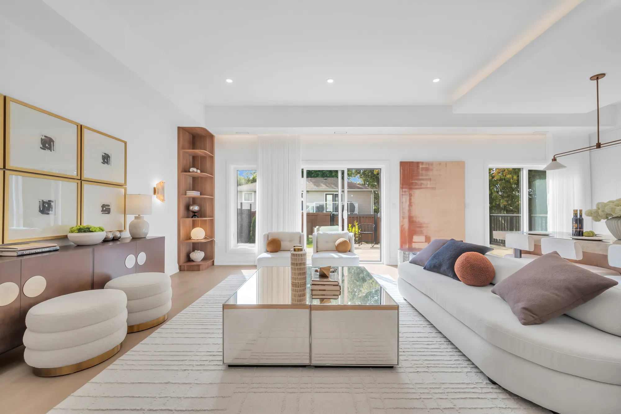 The living room from the kitchen: the sofas, the console with its prints and sconces, an oak shelf unit at the right, the deck doors