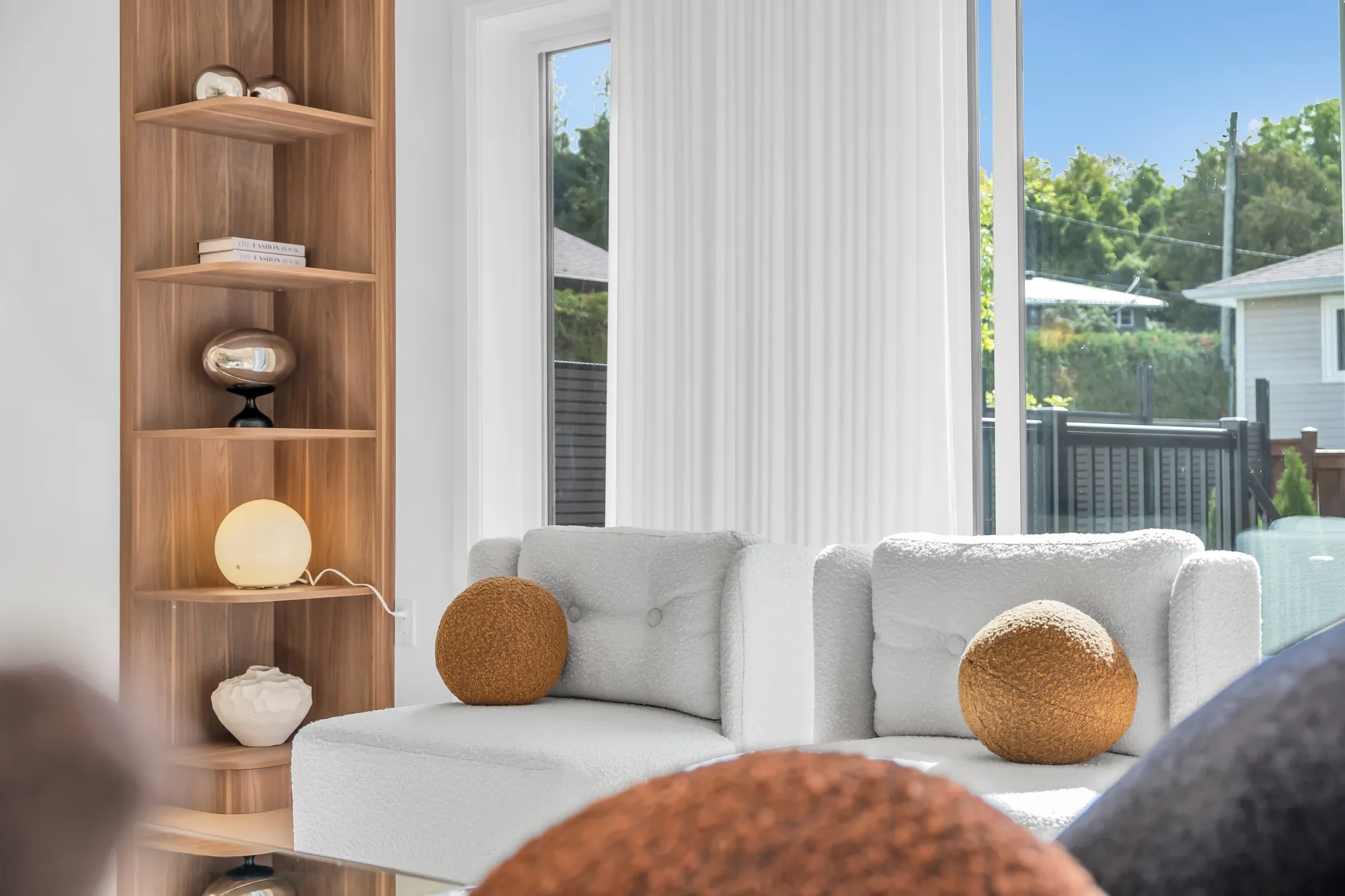 A detail of the living room: the oak shelf unit with a lamp and vases, the white sofa, the window and the trees beyond