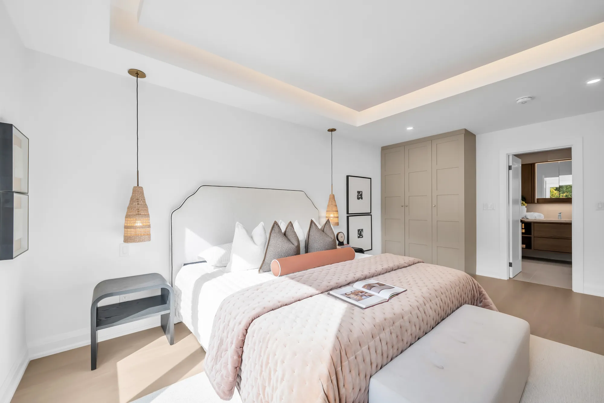 The primary bedroom from the door: the bed and the pendants, the tray ceiling, the doorway to the ensuite at the right