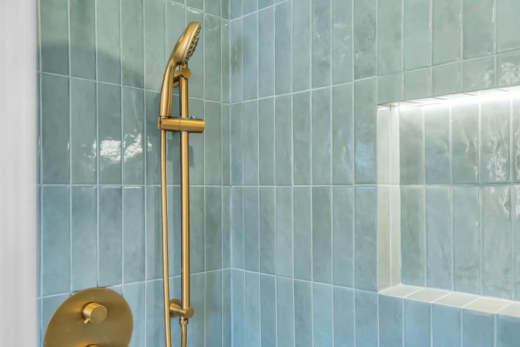 A detail of the green tile: the brass hand shower on its rail, the lit niche
