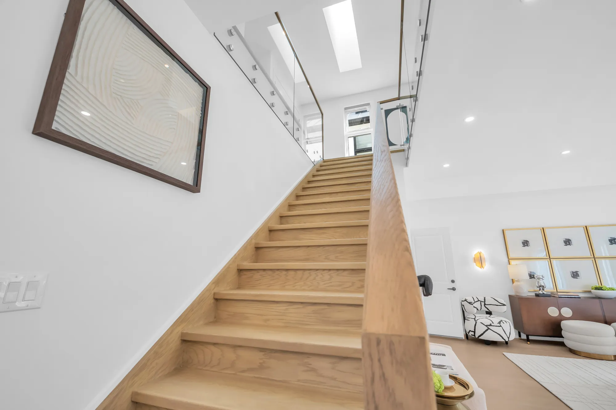 The stair from the foot: oak treads, a glass railing with an oak handrail, the landing above