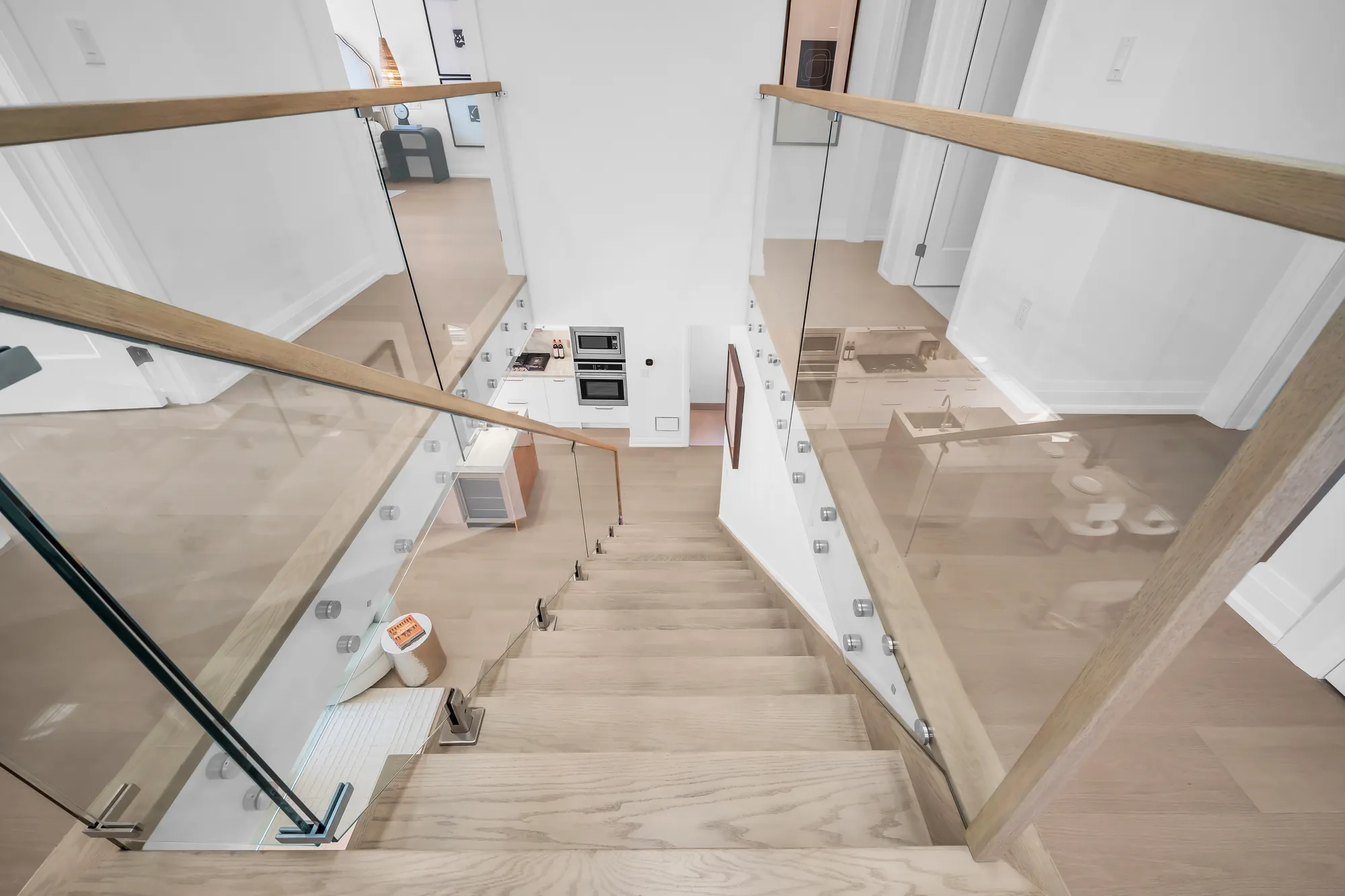 The stair from the landing: oak treads turning down behind glass panels, the foyer below