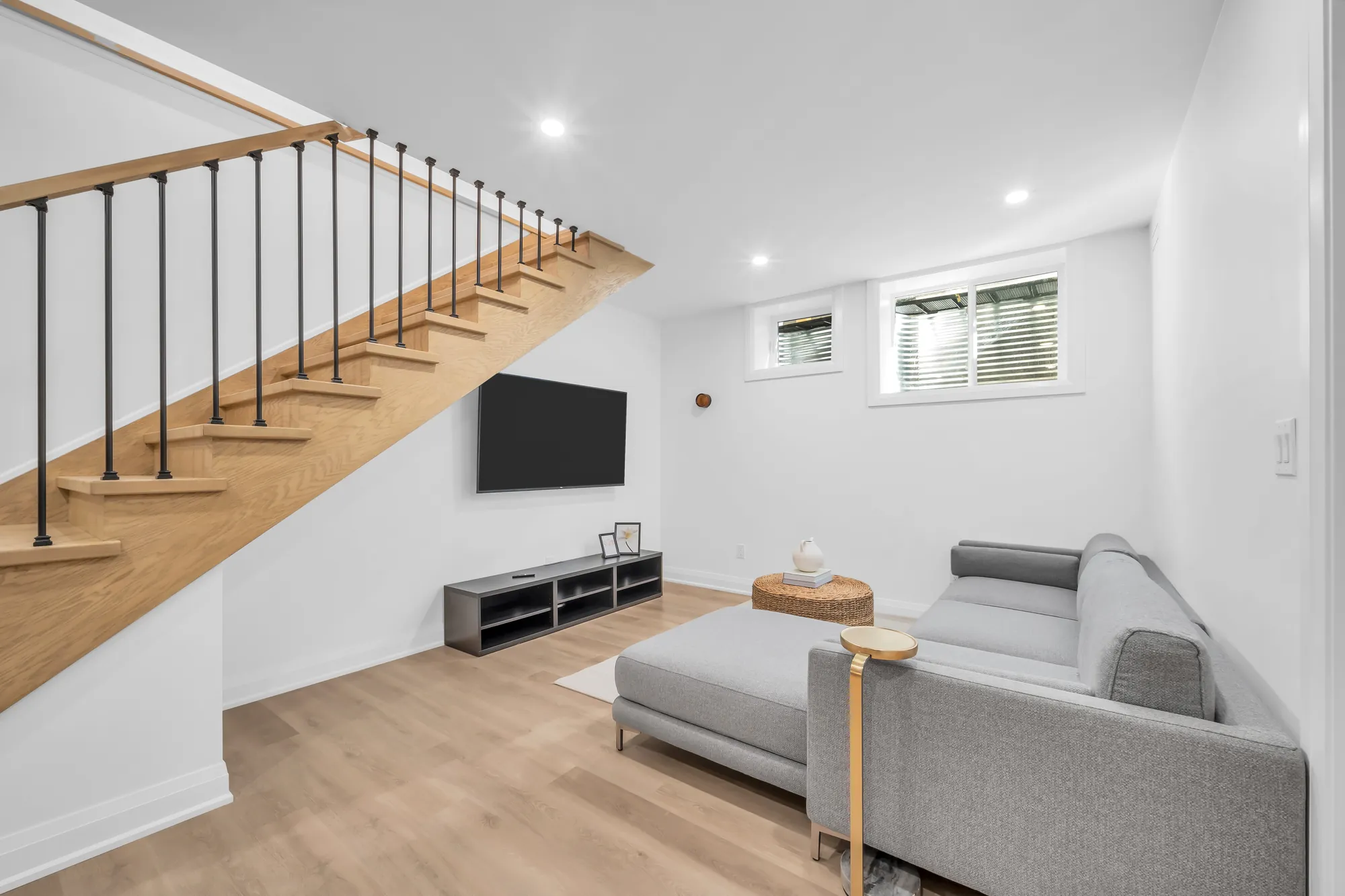 The lower level's living area: a grey sofa under the stair, a television and a console