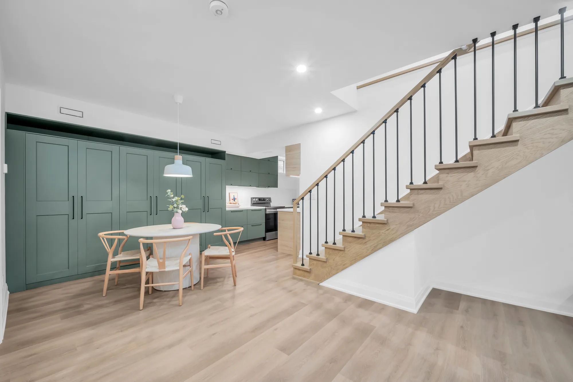 The lower level's kitchen and dining: sage green cabinets, a round white table with wood chairs, the stair