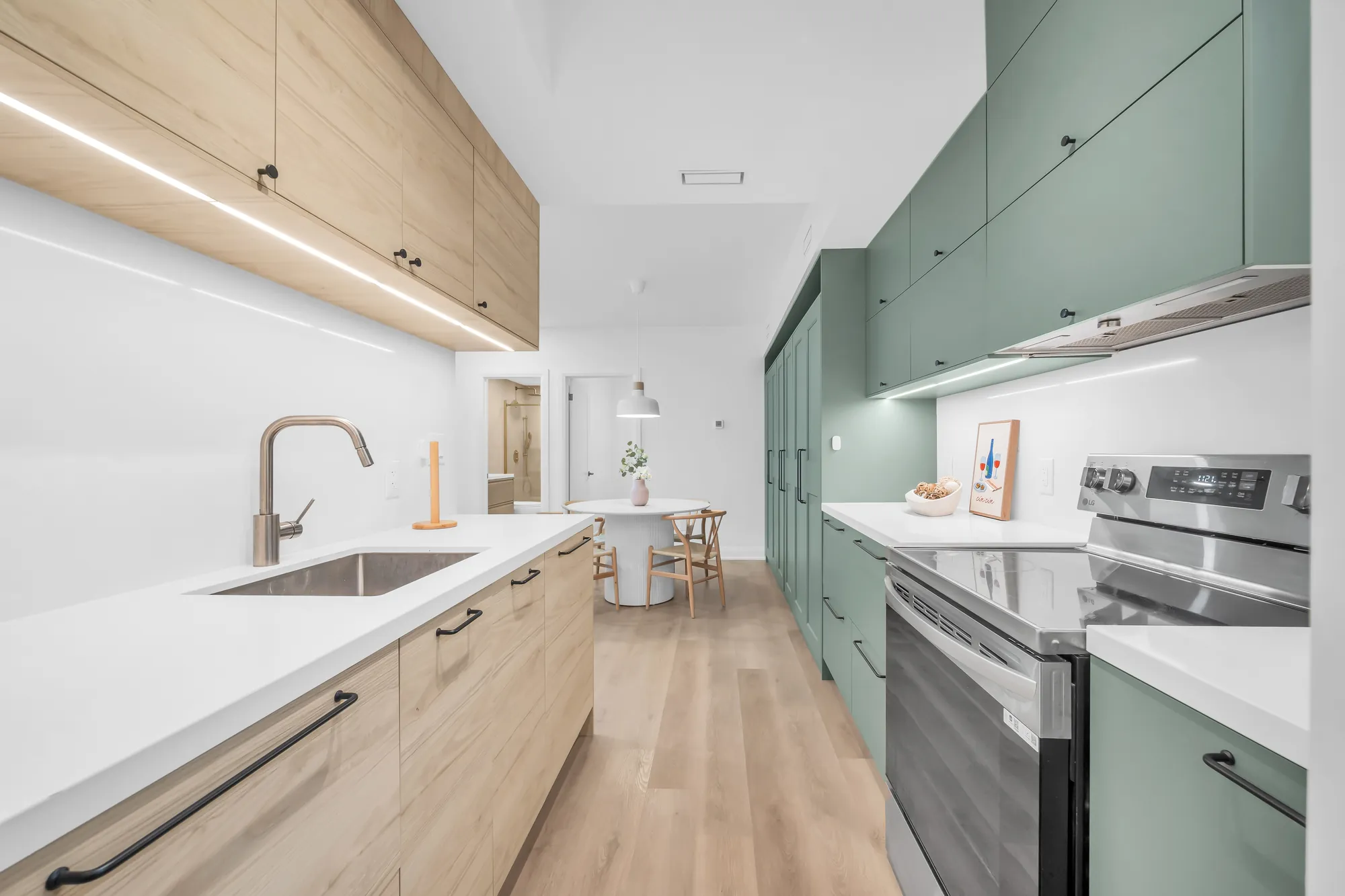 The lower level's kitchen along its counter: the sink and a brass tap, the range, the sage cabinets, the dining table beyond